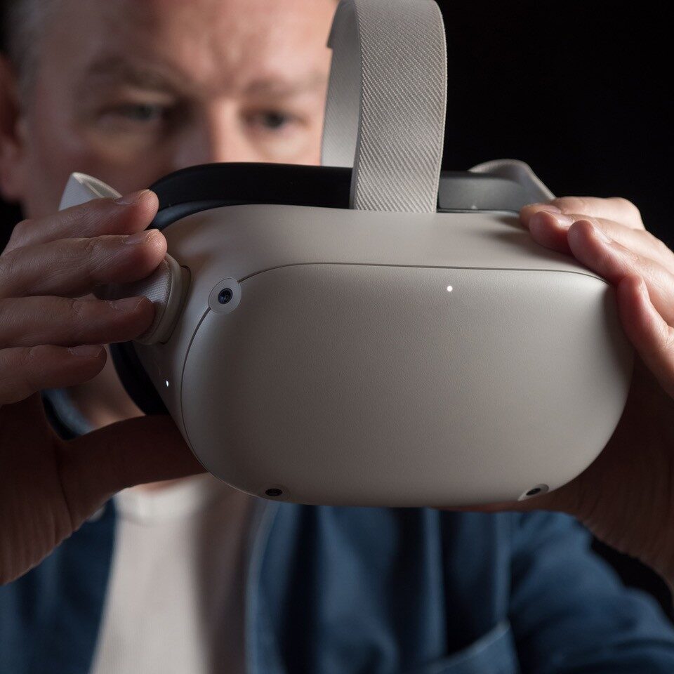 White man holds VR headset in his hands, he appears to be either putting on or taking off the headset.